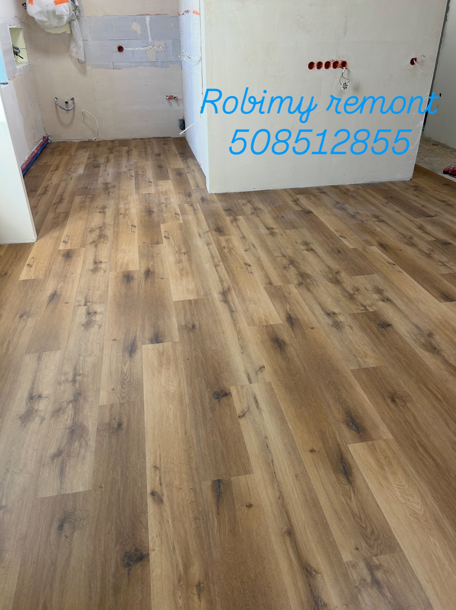 Ułożona podłoga z paneli w trakcie remontu kuchni. Widoczne przygotowane ściany z instalacjami. Panele w odcieniach brązu z wyraźną strukturą drewna.