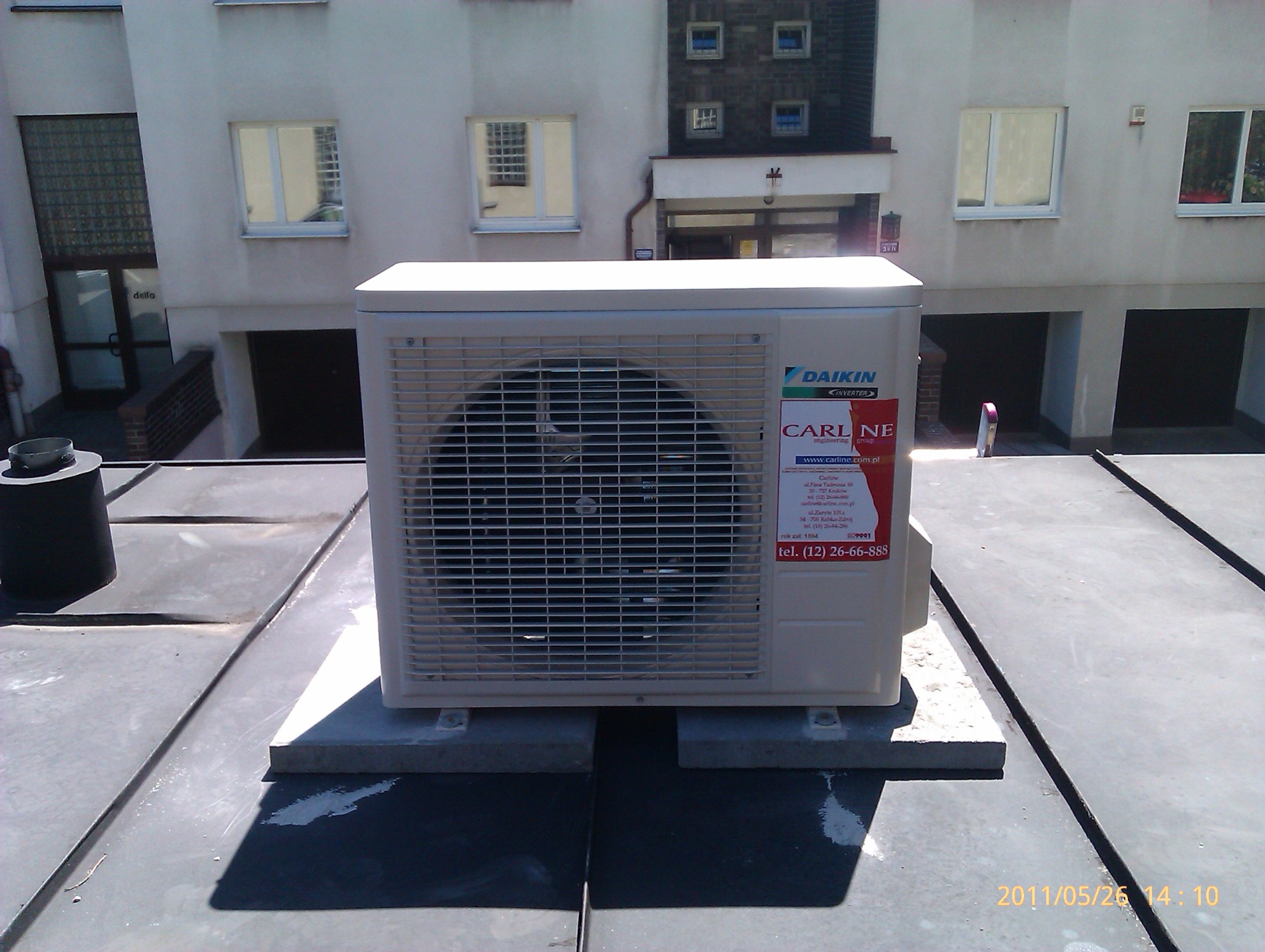 Zewnętrzna jednostka klimatyzacji marki Daikin, zamontowana na płaskim dachu budynku mieszkalnego, z widoczną naklejką firmy Carlne engineering group.