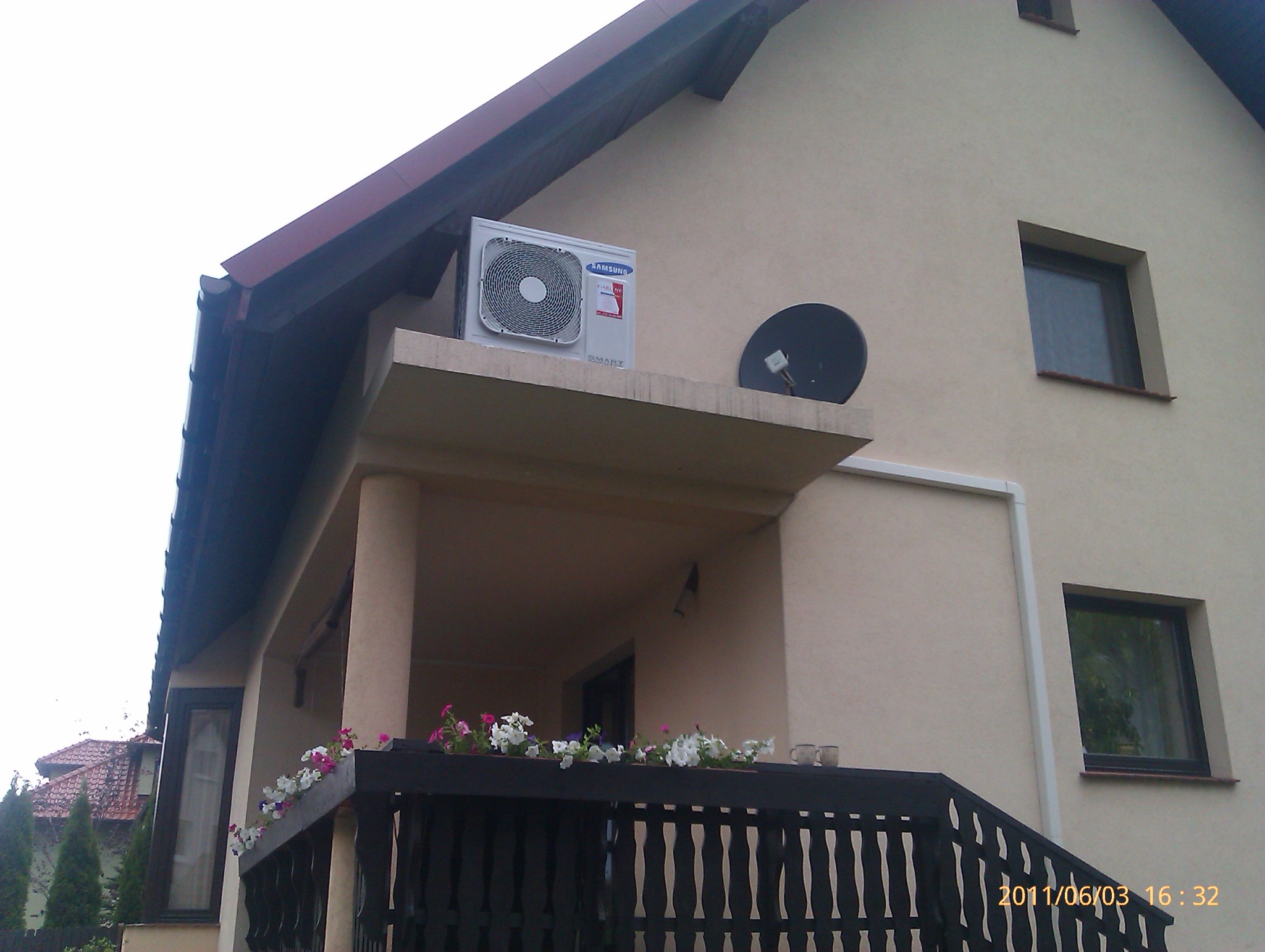 Zewnętrzna jednostka klimatyzacji Samsung zamontowana na balkonie domu jednorodzinnego, obok antena satelitarna.