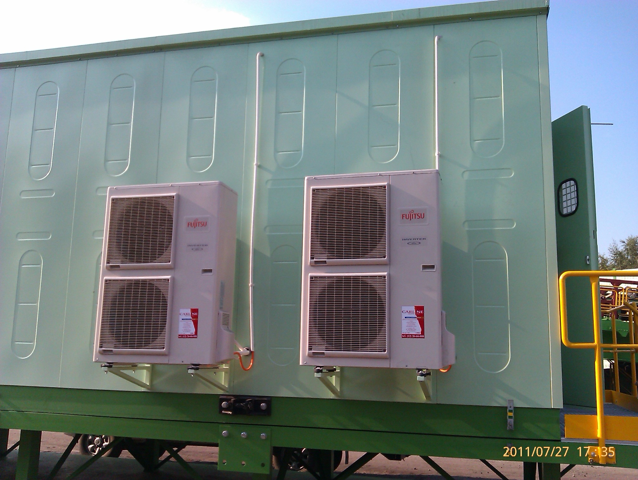 Dwa zewnętrzne agregaty klimatyzacji Fujitsu zamontowane na jasnym, zielonym kontenerze, z widocznymi rurami i wspornikami montażowymi.