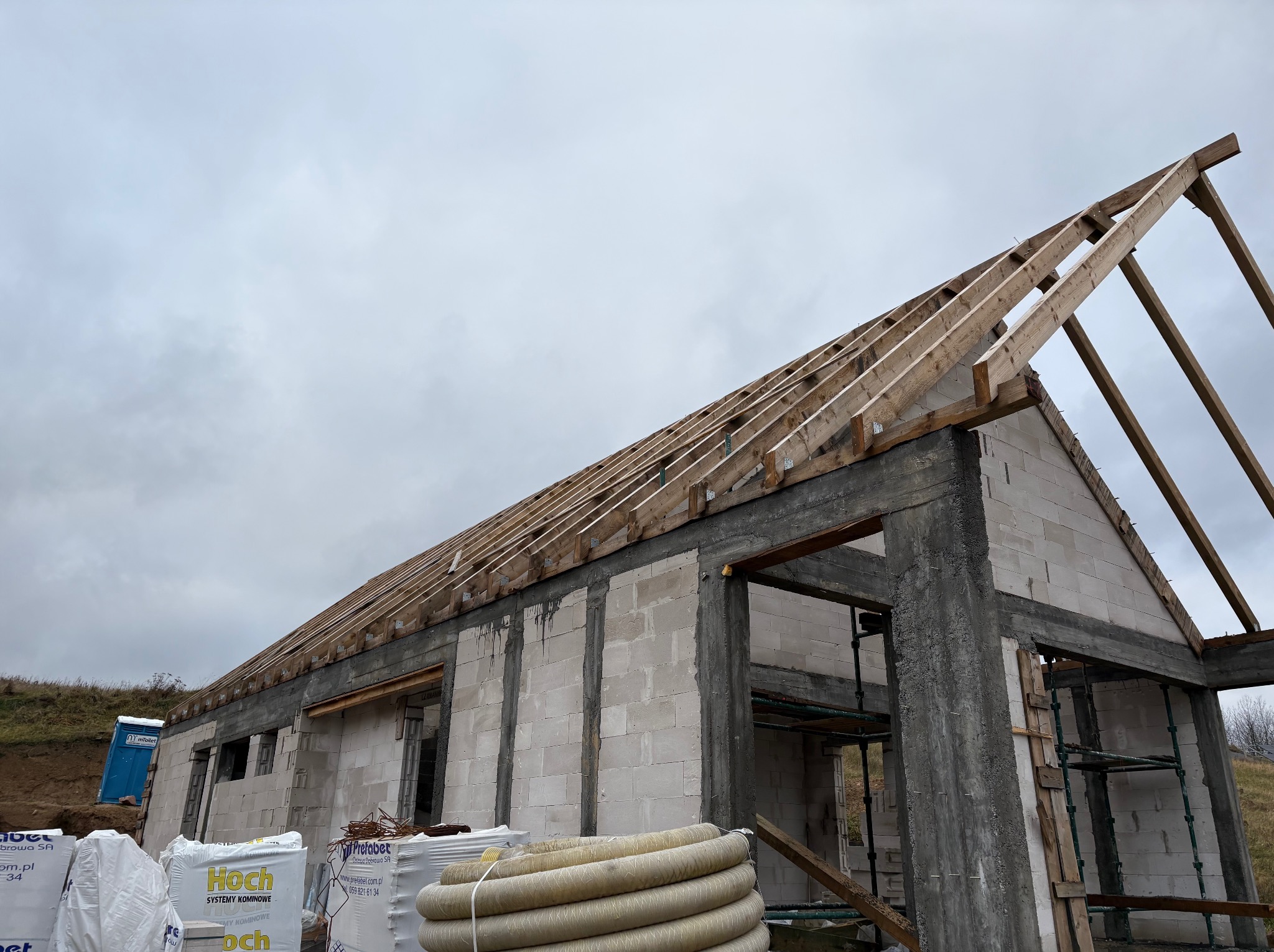Budowa domu jednorodzinnego w stanie surowym otwartym: ściany z betonu komórkowego, drewniana więźba dachowa, materiały budowlane na pierwszym planie.