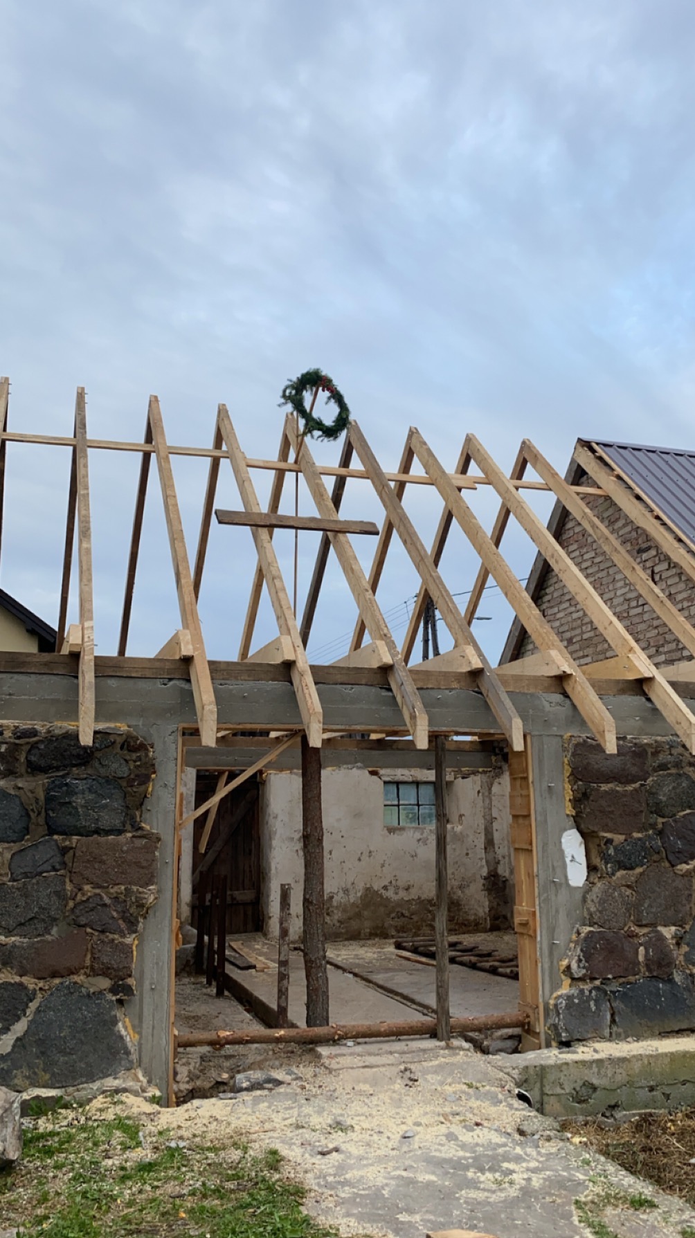 Wznoszenie więźby dachowej na budynku z kamiennymi ścianami, widoczny wieniec na dachu, surowy stan, pochmurne niebo.