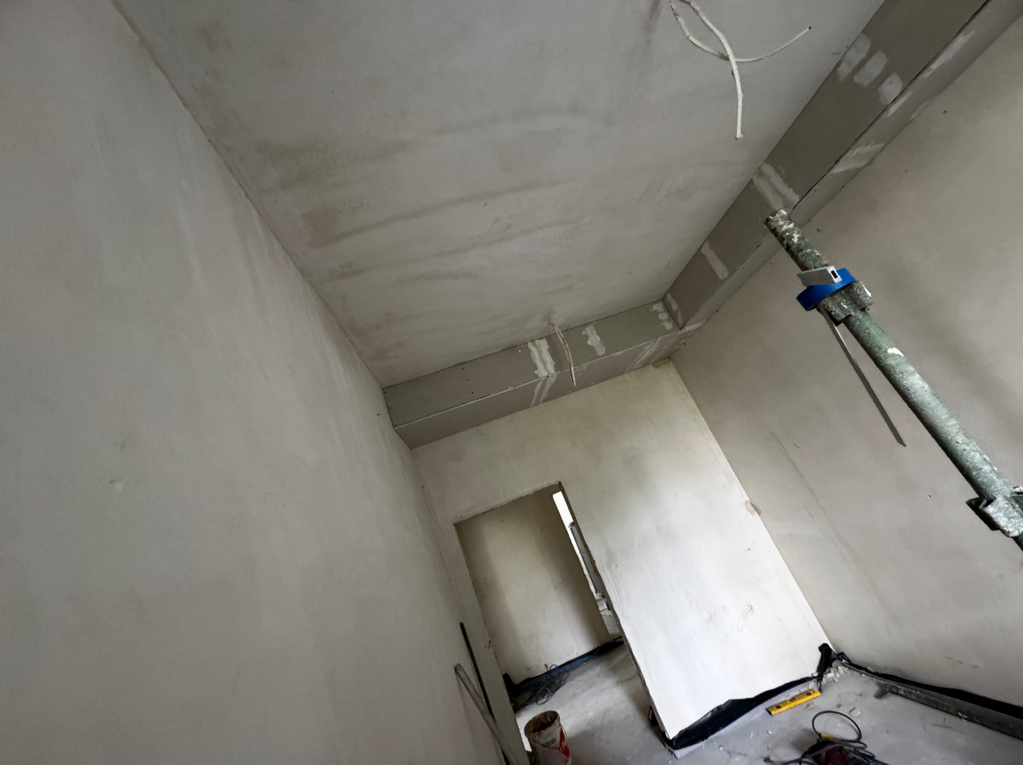 Wnętrze w trakcie prac wykończeniowych: ściany po szpachlowaniu, widoczne płyty gipsowe na suficie, podpora teleskopowa. Perspektywa z dołu.