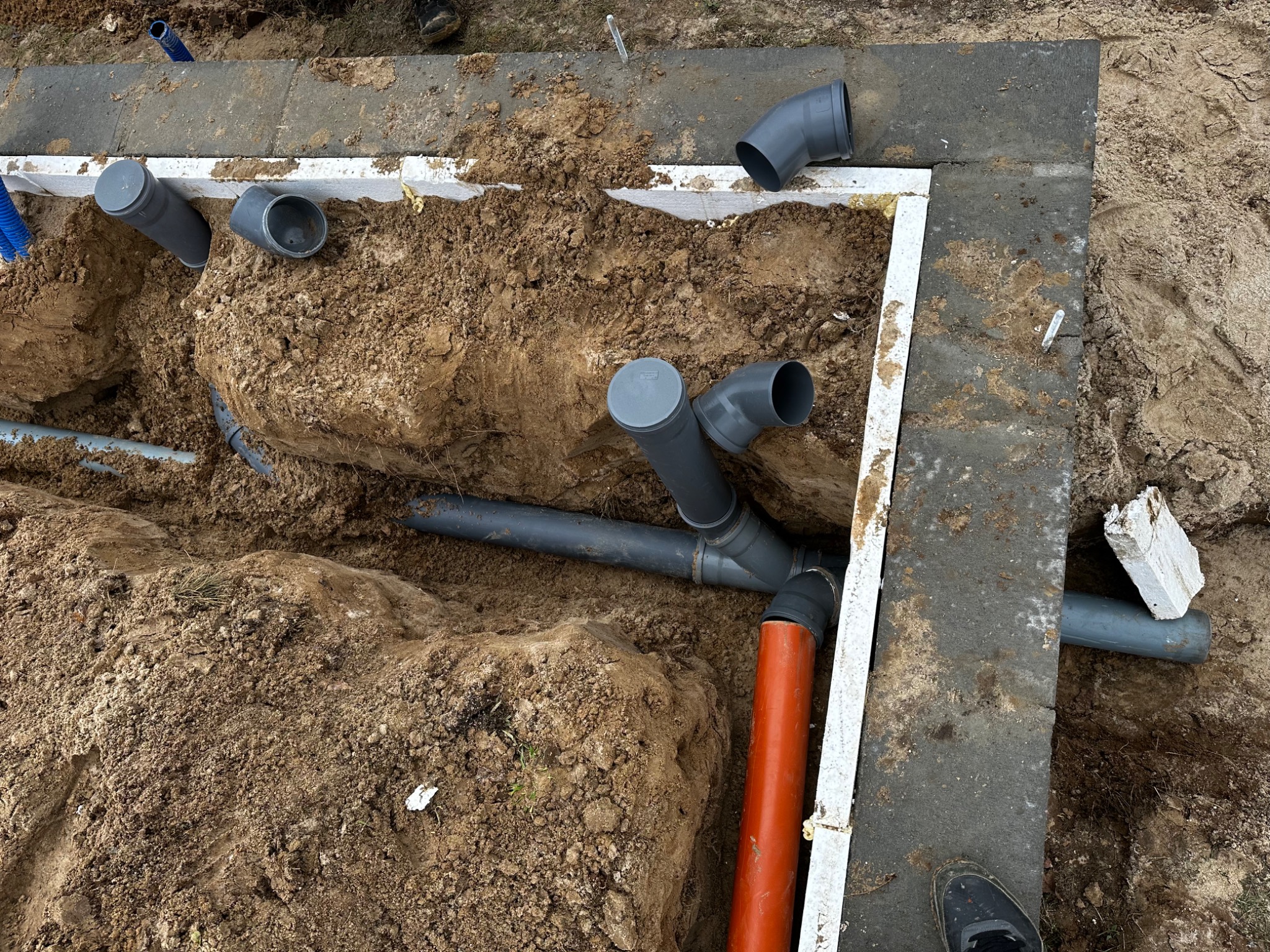 Montaż instalacji kanalizacyjnej w wykopie fundamentowym w Łochowie, widoczne rury kanalizacyjne z kształtkami w ziemi.