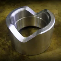 Metalowy pierścień z wycięciem w kształcie litery V, wykonany na tokarce, leżący na brązowym tle.