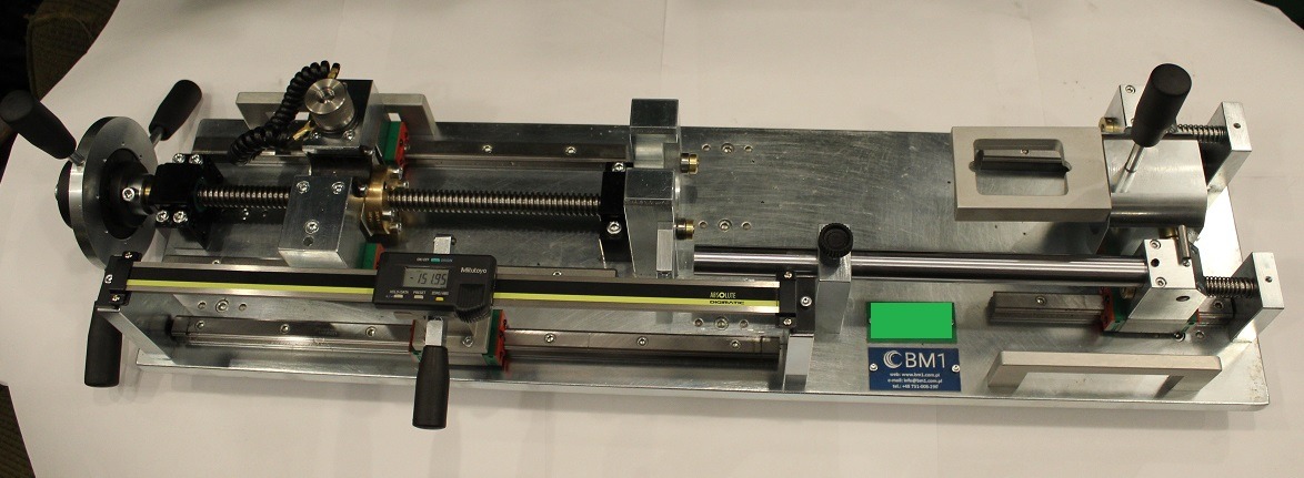 Metalowa konstrukcja tokarki z przekładnią śrubową, suwakiem i cyfrowym wyświetlaczem pomiaru, na jasnym tle.