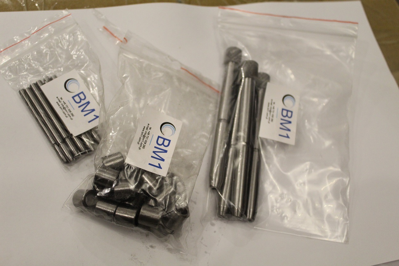 Zestaw precyzyjnie obrobionych, metalowych elementów zapakowanych w przezroczyste woreczki strunowe z etykietą firmy BM1.