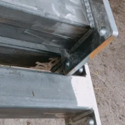 Dwa segmenty konstrukcji stalowej z przyspawanymi płytami montażowymi, widoczne spawy, surowy stan metalu, leżą na ziemi.