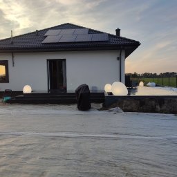 Marek Kołyt - Biały dom jednorodzinny z czarnym dachem i panelami słonecznymi w trakcie remontu, folia ochronna na trawniku, oświetlenie zewnętrzne w postaci kul.