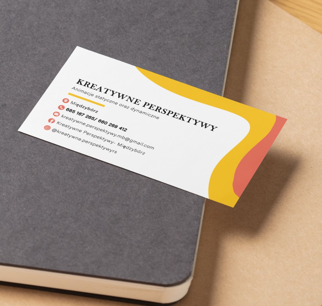 Wizytówka z grafiką w kolorach żółtym i koralowym na szarym notatniku. Minimalistyczny design z danymi kontaktowymi i nazwą firmy: Kreatywne Perspektywy.