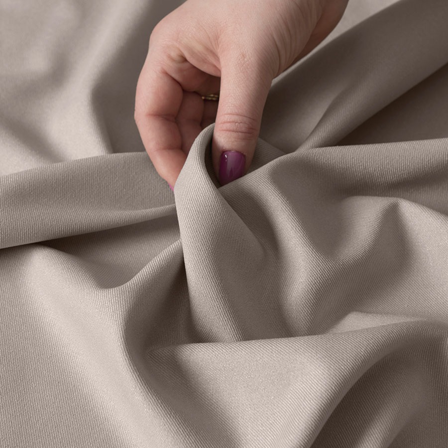Dłoń z fioletowym lakierem na paznokciach delikatnie unosi beżową tkaninę z widoczną teksturą splotu.