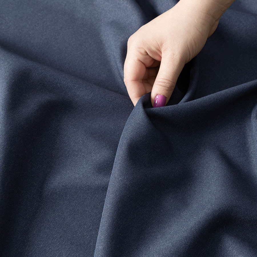 Dłoń kobiety z fioletowym lakierem na paznokciach dotyka fałd granatowej tkaniny o delikatnym połysku.