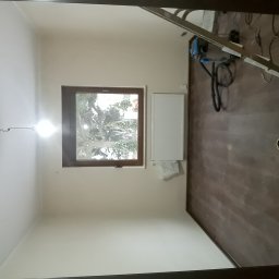 Prywatnie - Pokój w trakcie prac wykończeniowych: świeżo pomalowane ściany na biało, częściowo ułożone panele podłogowe, grzejnik zamontowany pod oknem, drabina oparta o ścianę, widoczne narzędzia i materiały...