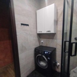 Prywatnie - Nowoczesna łazienka z beżowymi płytkami, czarną pralką Electrolux, białą szafką wiszącą i czarną kabiną prysznicową z widoczną armaturą.