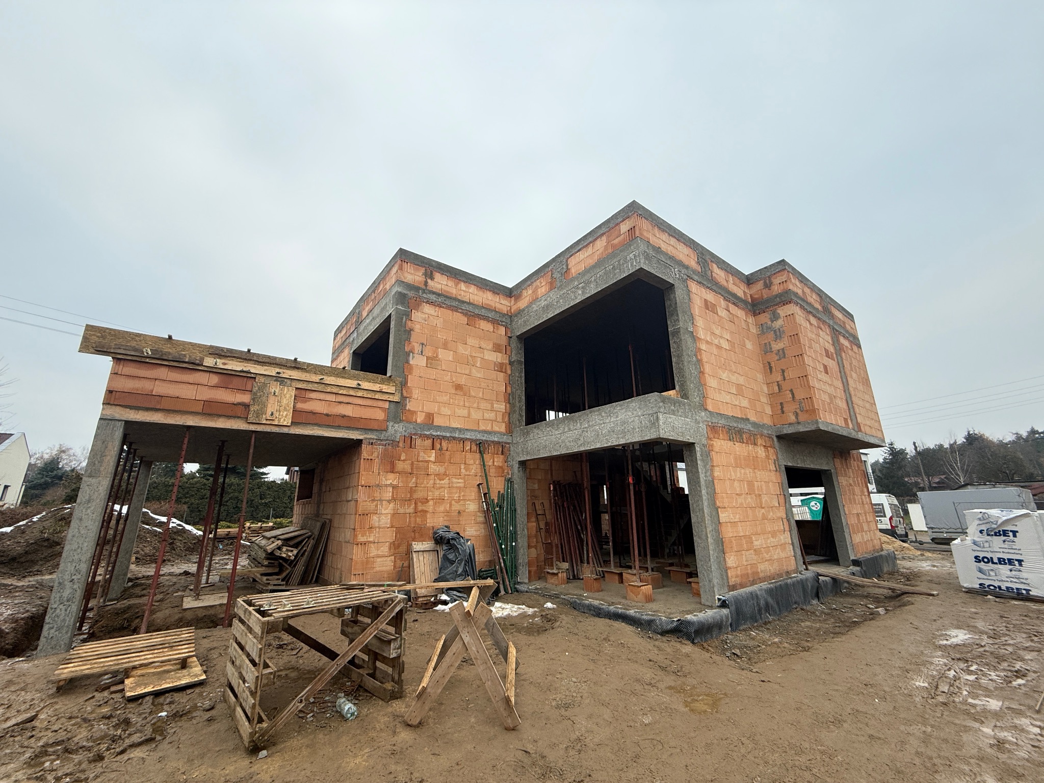 Surowy stan domu murowanego z betonu komórkowego w Czarnkowie. Widoczne pustaki i betonowe nadproża, szalunki, podpory. Budowa w toku, pochmurny dzień.