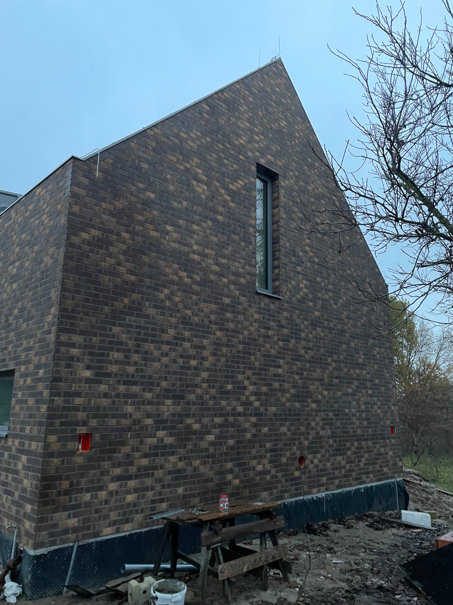 Nowoczesny dom murowany z ciemnej cegły w Czarnkowie, z pionowym oknem i widocznymi elementami wykończeniowymi wokół budynku.