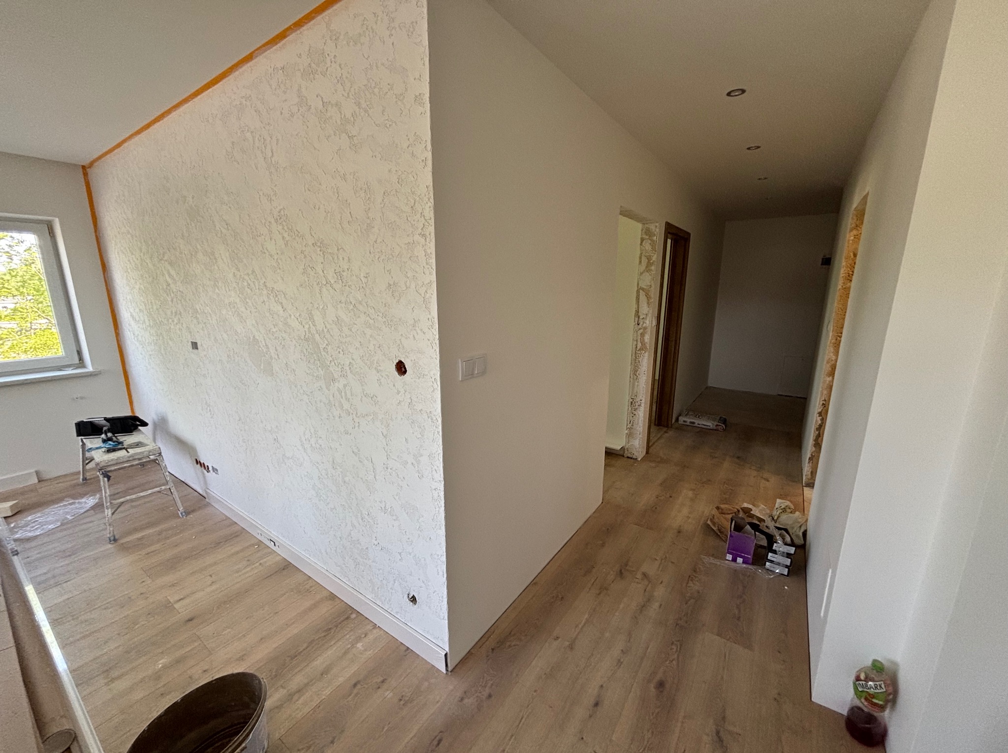 Wykończone wnętrze: ściana z dekoracyjną strukturą, drewnopodobna podłoga, listwy przypodłogowe. Widoczne narzędzia malarskie i schody malarskie.