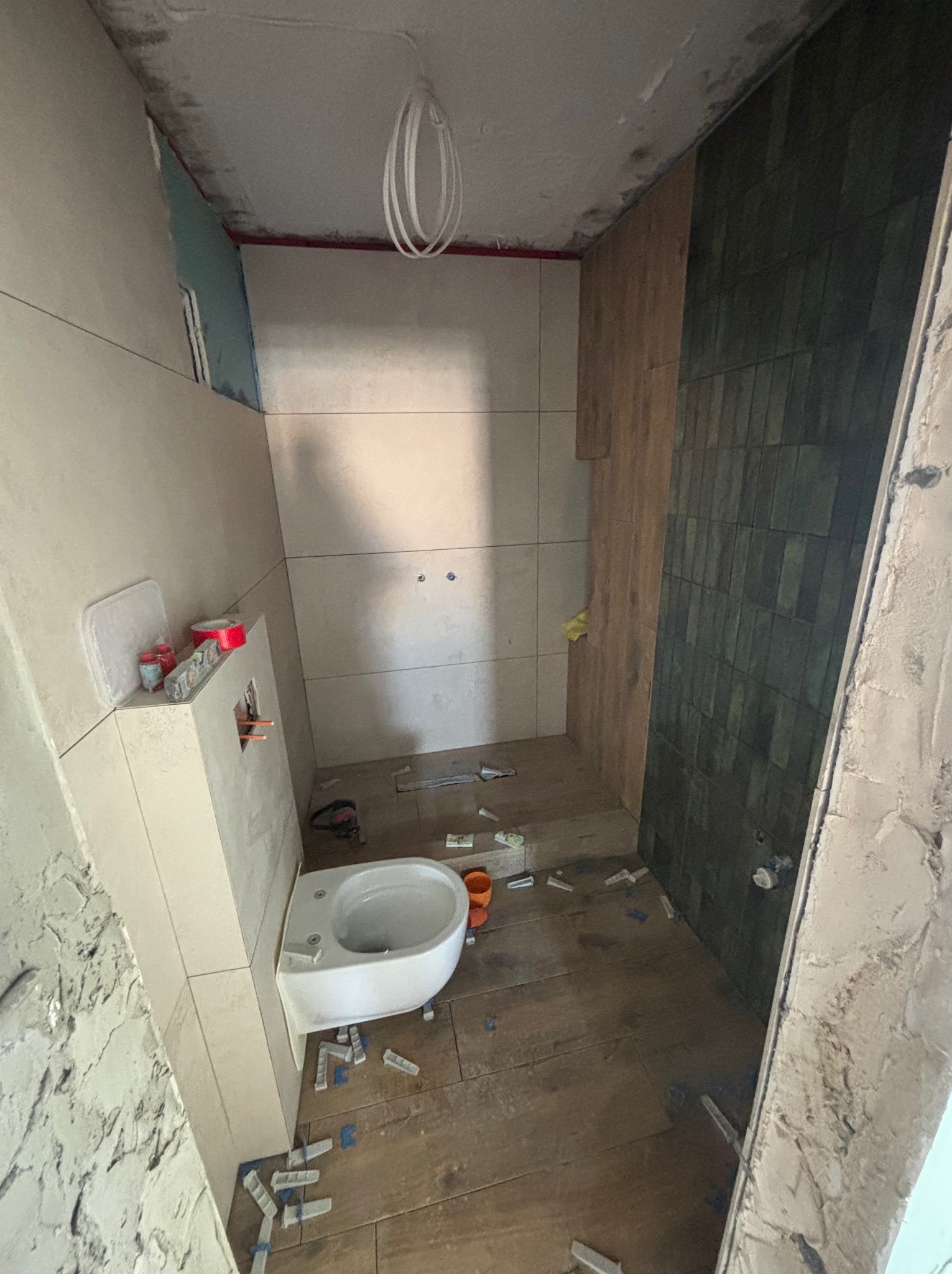 Wnętrze łazienki w trakcie remontu: częściowo wyłożone płytki na ścianach, podwieszana toaleta, widoczne narzędzia i materiały budowlane. Ujęcie z bliska.