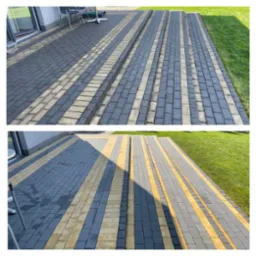 Ułożona kostka brukowa w dwóch odcieniach szarości z żółtymi pasami, tworząca chodnik i schody przed domem z trawnikiem w tle.