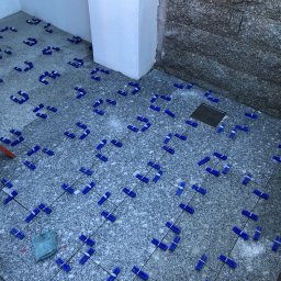 K-Maro - Granitowa posadzka w trakcie układania, z użyciem niebieskich klipsów poziomujących i sznurka, widoczny odpływ liniowy i szmatka do czyszczenia.