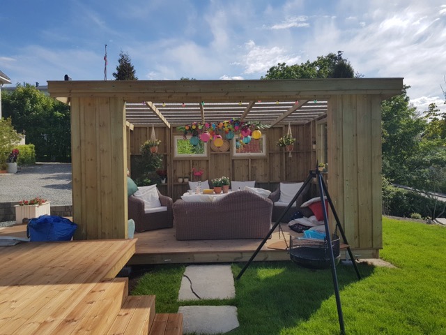 Drewniana altana z tarasem i meblami ogrodowymi, dekorowana kolorowymi lampionami, z widokiem na bujną zieleń ogrodu.