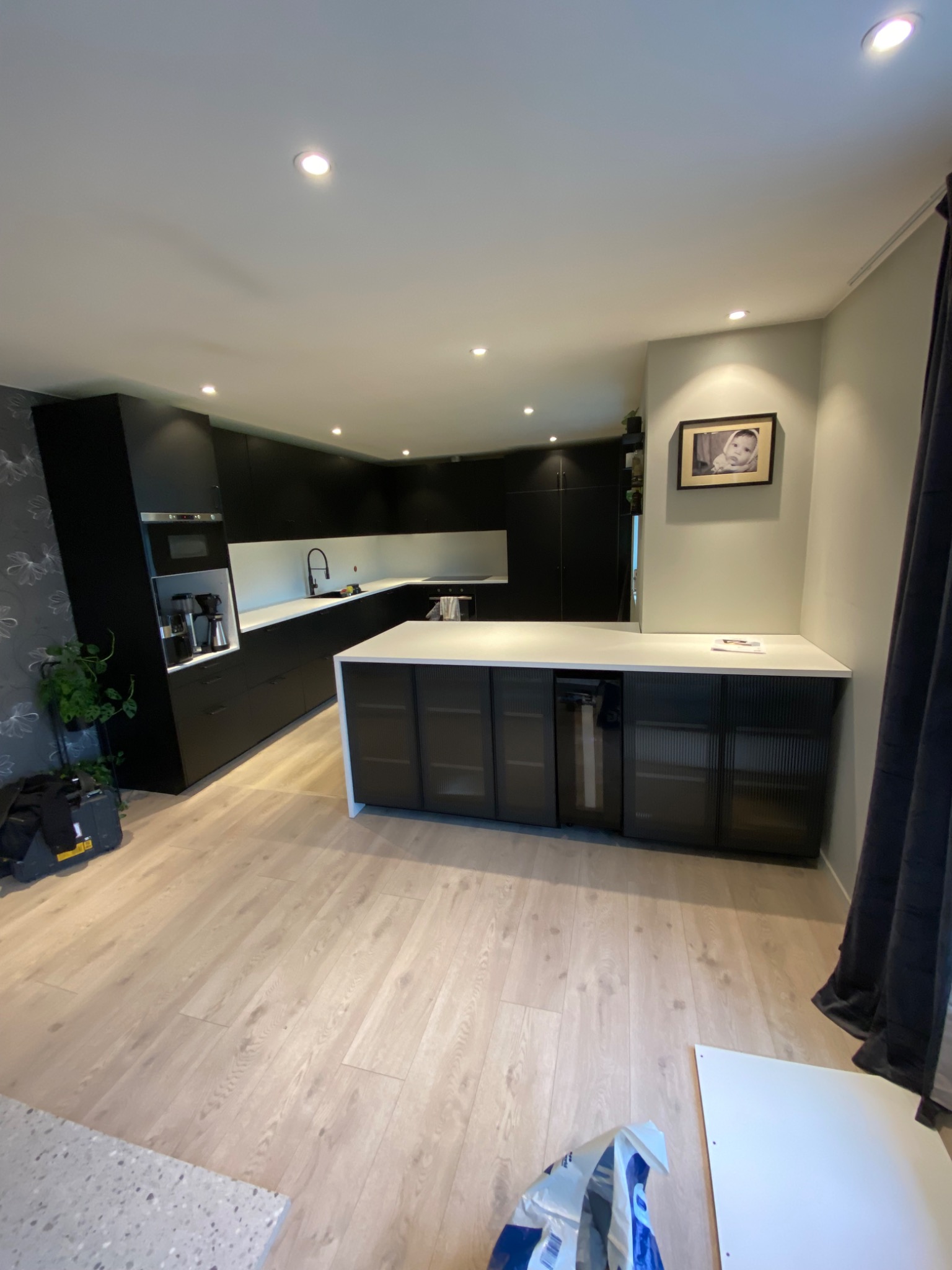 Nowoczesna kuchnia z czarnymi szafkami, białym blatem i wyspą kuchenną z ryflowanymi frontami, jasna drewniana podłoga, zdjęcie z szerokiego kąta.