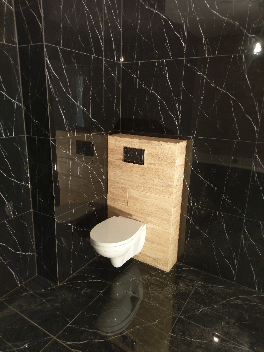 Nowoczesna toaleta podwieszana z drewnopodobną obudową stelaża, otoczona czarnymi płytkami imitującymi marmur w łazience w Katowicach.