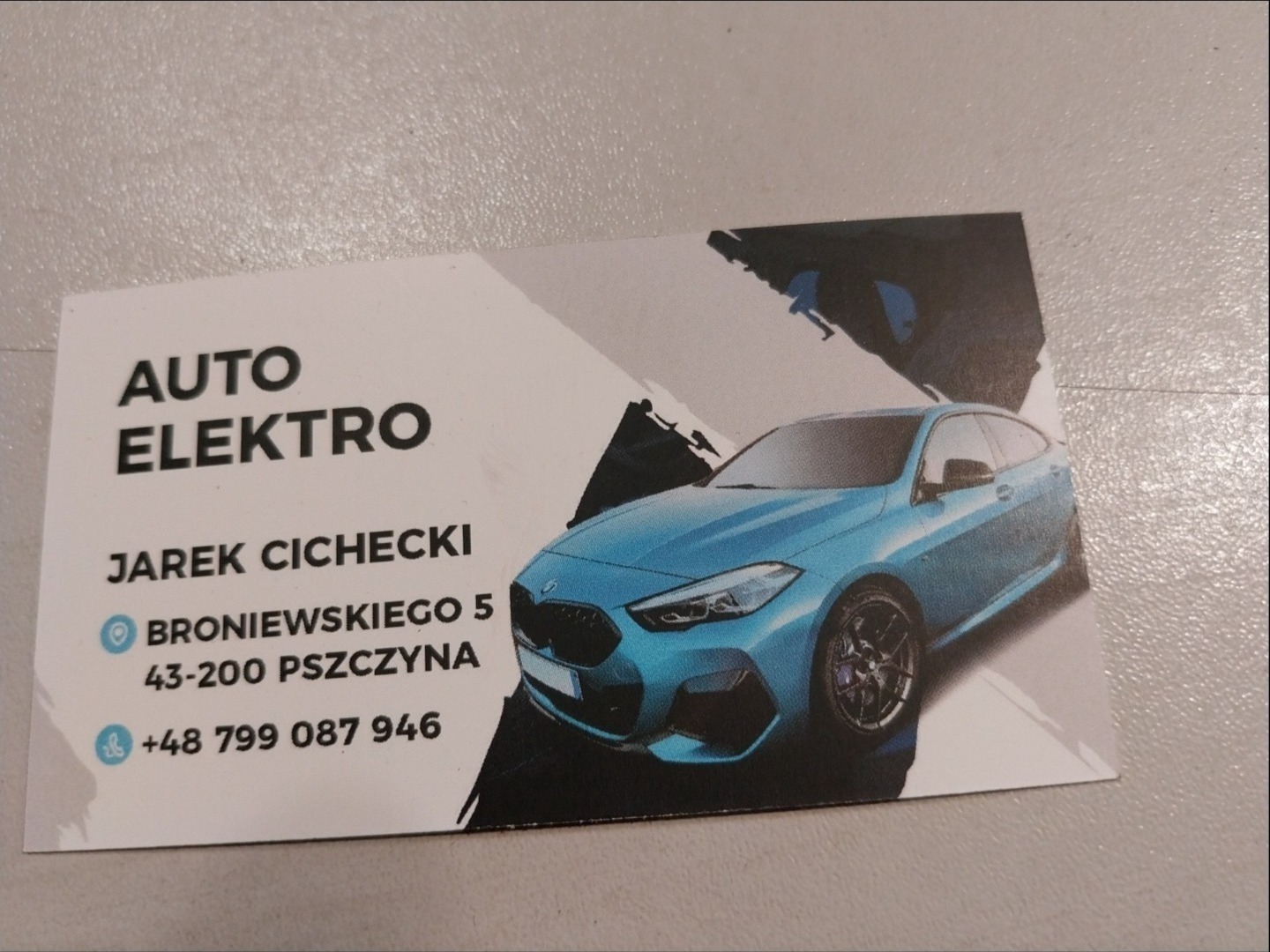 Wizytówka firmy Auto Elektro z błękitnym samochodem, adresem Broniewskiego 5 w Pszczynie i numerem telefonu +48 799 087 946.