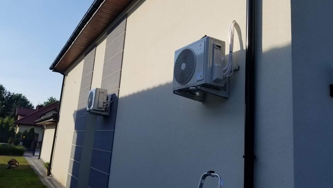 Dwa zewnętrzne moduły klimatyzacji zamontowane na elewacji domu jednorodzinnego z widoczną drabiną, sugerującą niedawny montaż.