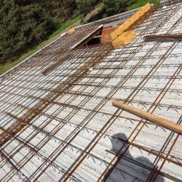 Mateusz Szkopiak Usługi Budowlane - Zbrojenie płyty fundamentowej z widocznym deskowaniem, w tle drzewa i cień osoby.