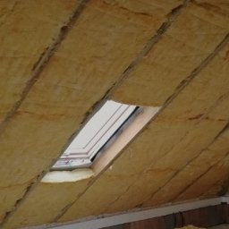 Mateusz Szkopiak Usługi Budowlane - Ocieplone wełną mineralną poddasze z oknem dachowym, widoczna konstrukcja więźby dachowej i fragment drabiny.