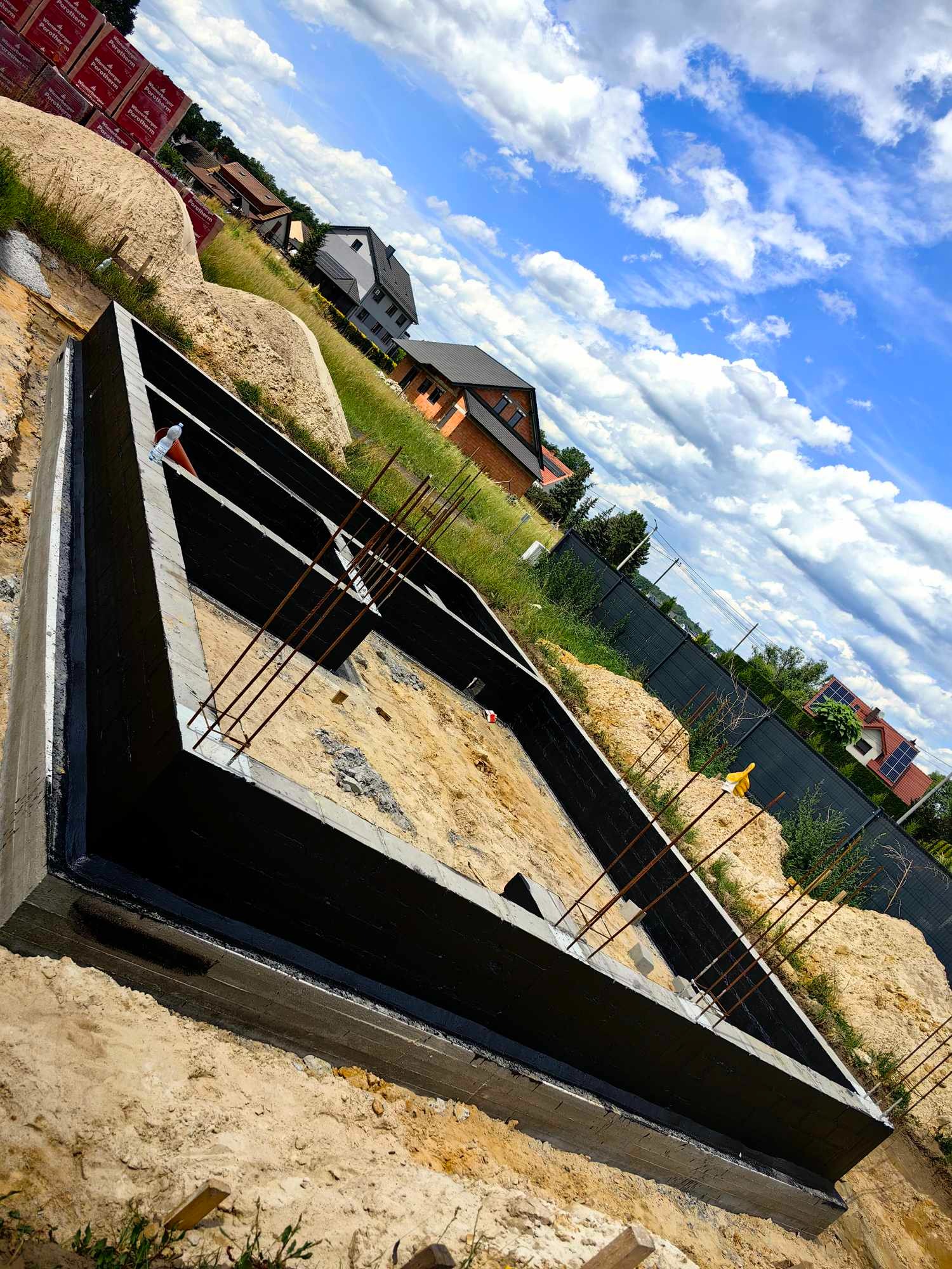 Zalane fundamenty pod budowę domu w Wołczynie, zbrojenie wystaje ponad poziom betonu, widoczne bloczki Porotherm w tle.