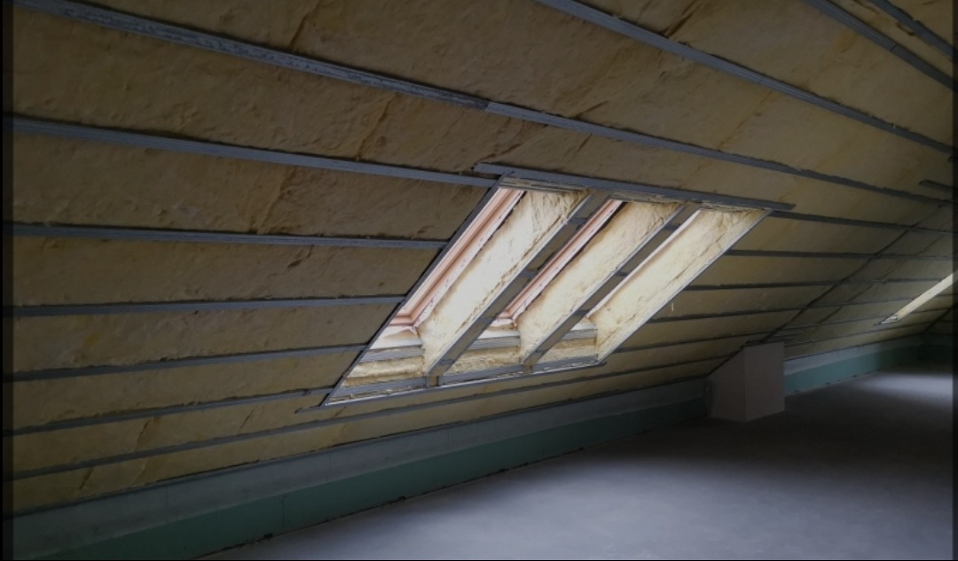 Poddasze z ociepleniem z wełny mineralnej, widoczne metalowe profile i okno dachowe w trakcie montażu.