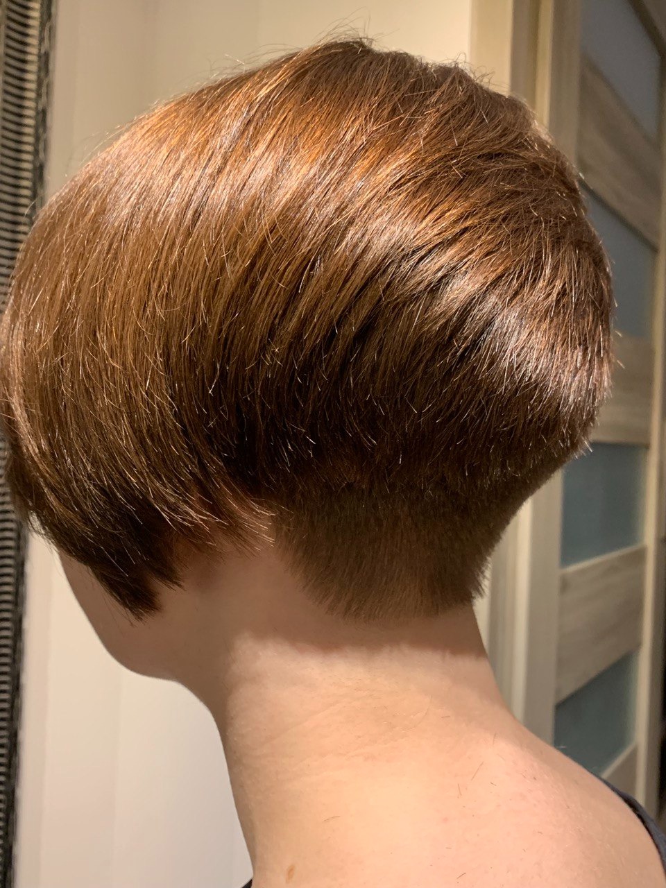 Krótkie, brązowe włosy z podgolonym tyłem głowy, widoczne z profilu, oświetlone światłem mieszanym.