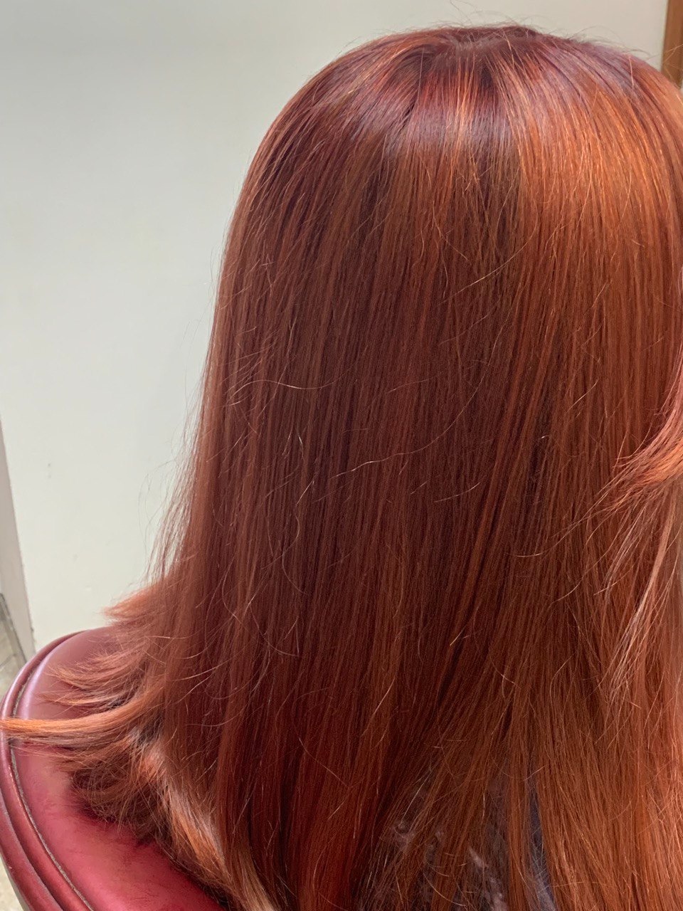 Ciemnorude, proste włosy z subtelnymi refleksami, widoczne z tyłu głowy, oparte o bordowe oparcie fotela.