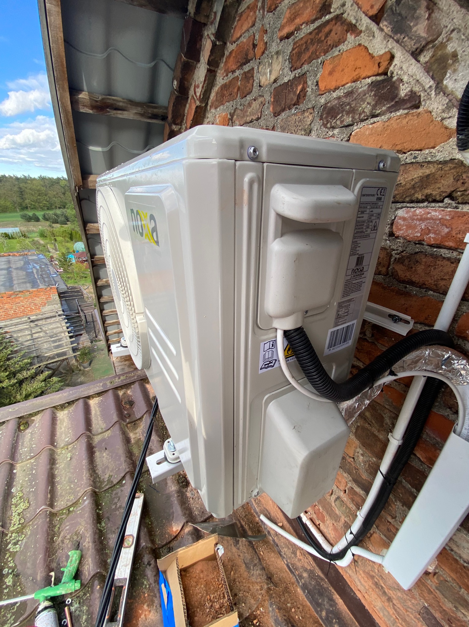 Zamontowana jednostka zewnętrzna klimatyzacji Nova na ceglanej ścianie budynku, widok z góry, z widocznymi narzędziami i elementami instalacji na dachu.