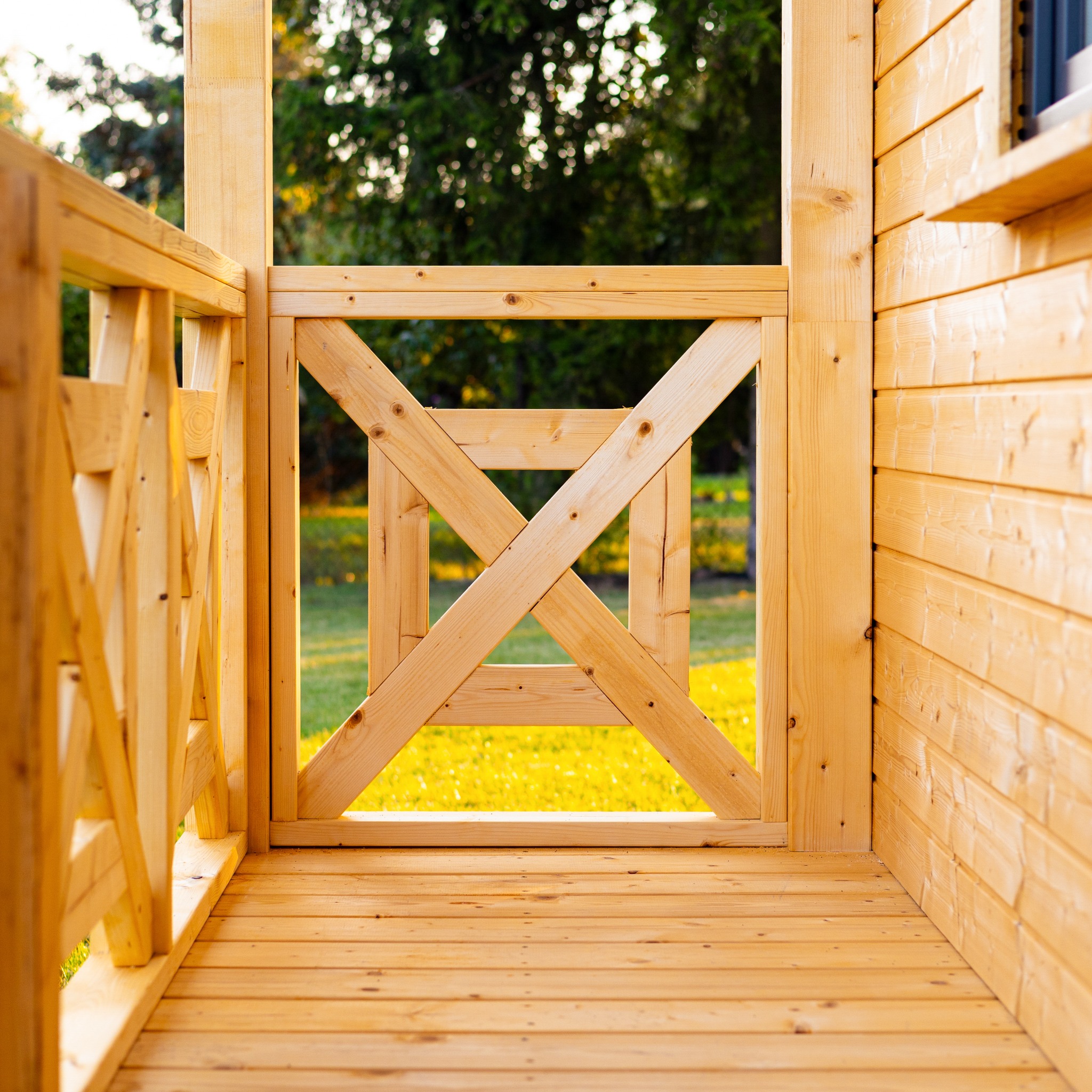 Wnętrze nowej, drewnianej altany z widokiem na trawnik przez dekoracyjne, krzyżowe panele balustrady.