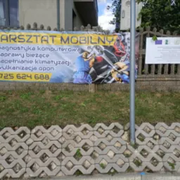 Baner reklamowy mobilnego warsztatu samochodowego z numerem telefonu, diagnostyką komputerową, naprawami bieżącymi, napełnianiem klimatyzacji i wulkanizacją opon, umieszczony na betonowym ogrodzeniu.