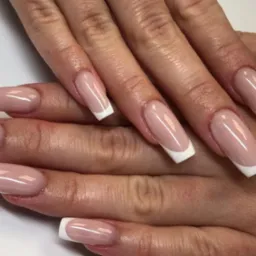 Dłonie z klasycznym, jasnoróżowym manicure francuskim na kwadratowych paznokciach, widoczne drobne zmarszczki na skórze dłoni.