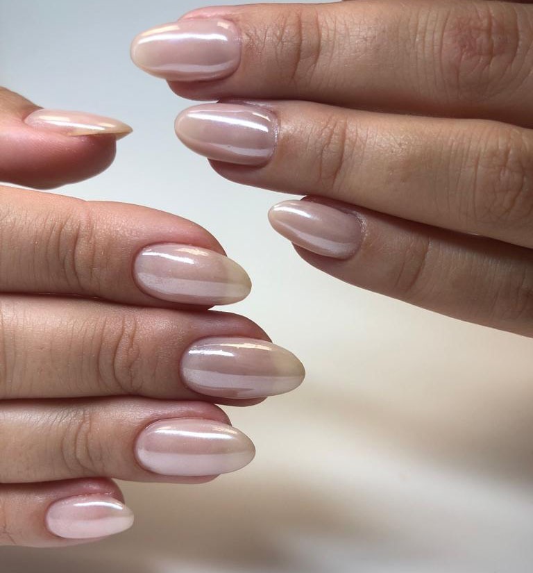 Dłonie z owalnymi paznokciami pomalowanymi na perłowy, beżowy odcień, widoczne delikatne refleksy światła.