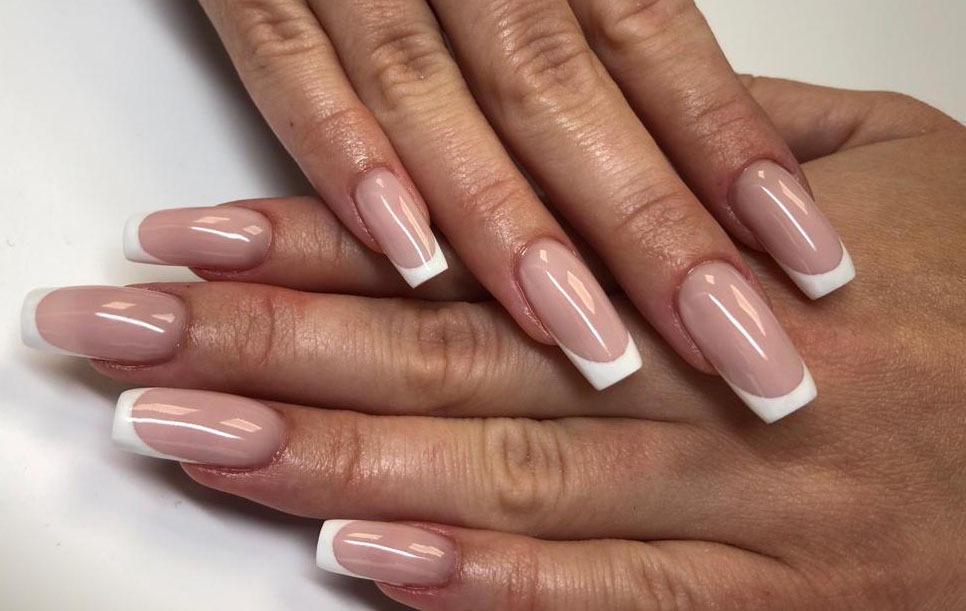 Dłonie z klasycznym, jasnoróżowym manicure francuskim na kwadratowych paznokciach, widoczne drobne zmarszczki na skórze dłoni.