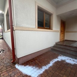 K-BUD Krystian Ujazdowski - Piana czyszcząca na kostce brukowej przed wejściem do domu z numerem 16, widoczny róg budynku z oknem i rynną.