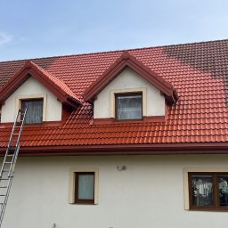 K-BUD Krystian Ujazdowski - Częściowo oczyszczony dach z czerwonej dachówki, widoczna drabina oparta o okno na poddaszu, kontrast między umytą a zabrudzoną powierzchnią dachu.