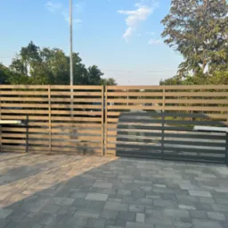 Automatyczna brama wjazdowa z poziomymi przęsłami, zamontowana na betonowych słupkach, z widocznym napędem i kostką brukową na podjeździe.