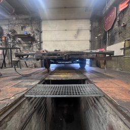 professional mobile welder PMWelders - Warsztat ślusarski: rama przyczepy na kanale, spawarka i narzędzia w tle. Surowy, industrialny klimat.