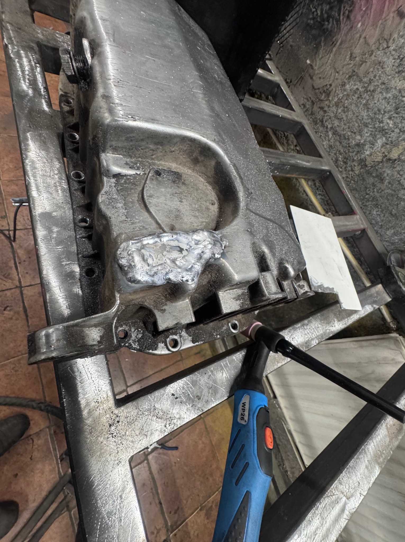 Spawanie elementu metalowego z widocznym spawem i uchwytem spawalniczym WP26 na warsztatowym stole. Obróbka metalu w trakcie realizacji.