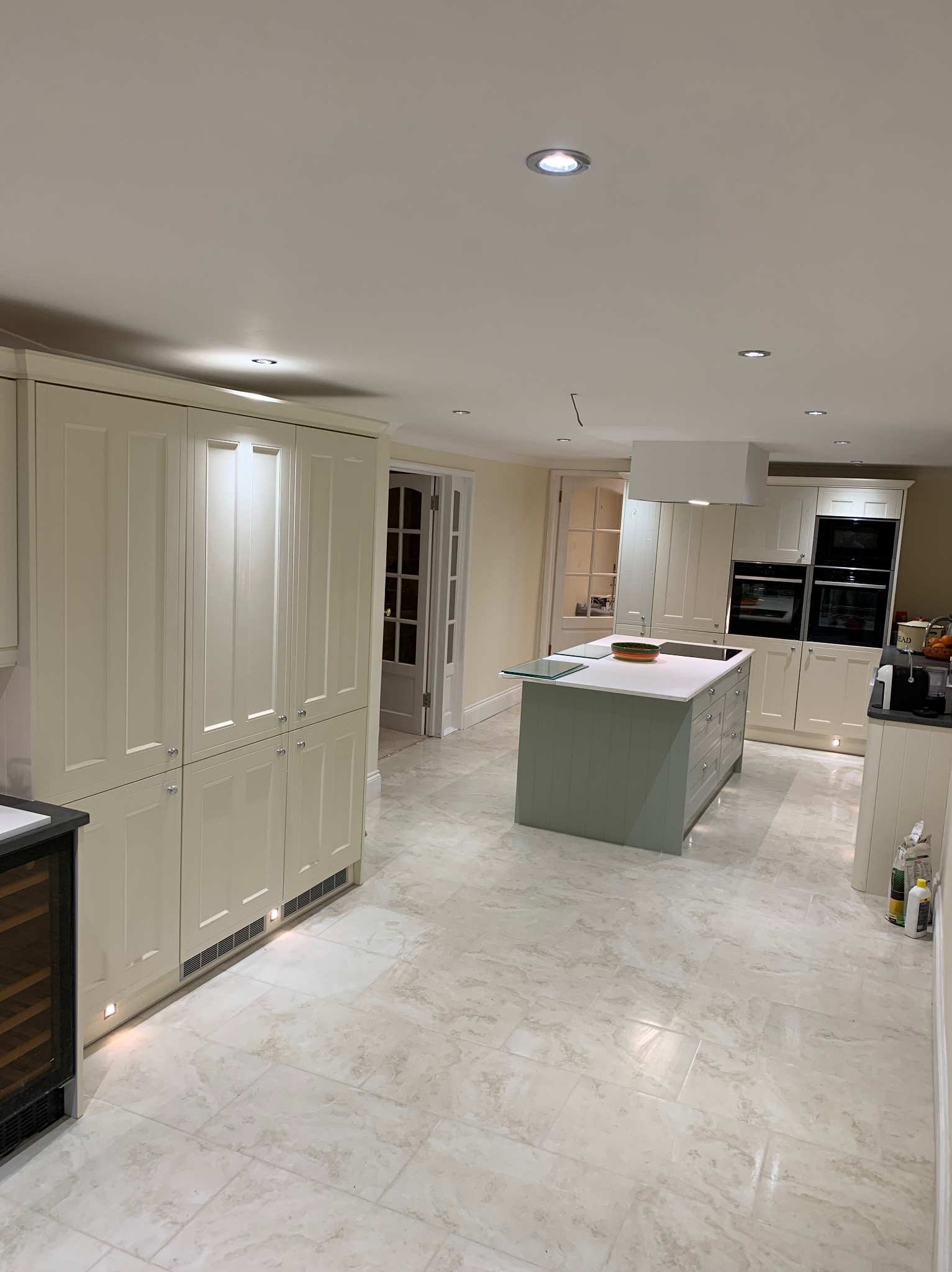 Jasna, przestronna kuchnia z wyspą w odcieniach zieleni i beżu, marmurowa podłoga i zabudowa kuchenna z oświetleniem punktowym.