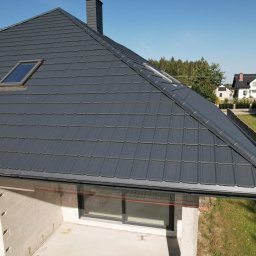 ŚWIAT DACHOW SAMBURSKI SPÓŁKA Z OGRANICZONĄ ODPOWIEDZIALNOŚCIĄ - Nowy, grafitowy dach z blachy trapezowej na domu w trakcie budowy, widoczne okna dachowe i orynnowanie, w tle dom jednorodzinny i zieleń.