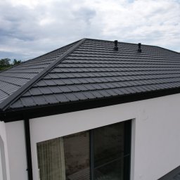 ŚWIAT DACHOW SAMBURSKI SPÓŁKA Z OGRANICZONĄ ODPOWIEDZIALNOŚCIĄ - Czarny dach z blachy trapezowej na nowoczesnym, białym domu jednorodzinnym, widok z góry, z widocznymi rynnami i kominami.