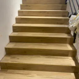 Schody wyłożone panelami imitującymi drewno, widok z dołu, zabezpieczone folią elementy wykończeniowe.